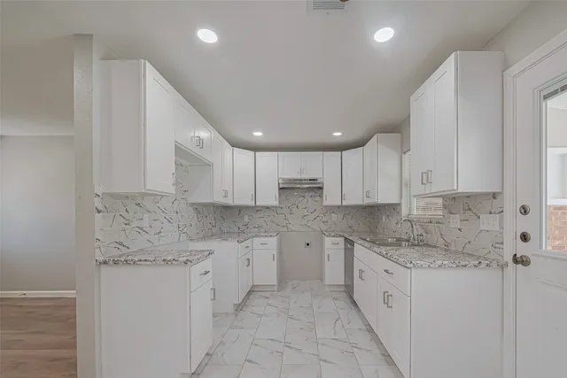 a kitchen that has a lot of white cabinets and stainless steel appliances