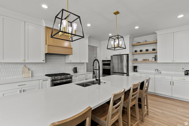 3111 South 1250 West Logan, UT 84321 - Photo 9 of 51 Spacious kitchen featuring an expansive central island with integrated double sink, white cabinetry, a large range with a wood-finish vent hood, a full-size stainless steel refrigerator, and wood-finish flooring