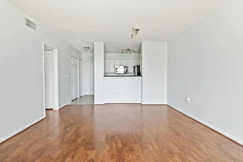 a view of a refrigerator in kitchen and an empty room with wooden floor