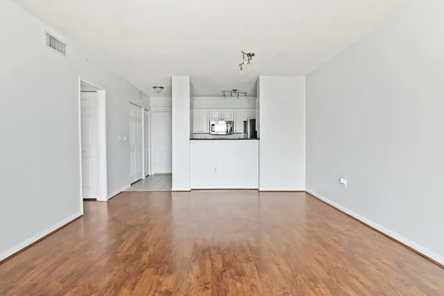 a view of a refrigerator in kitchen and an empty room with wooden floor
