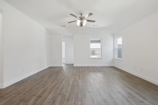 an empty room with wooden floor chandelier fan and windows