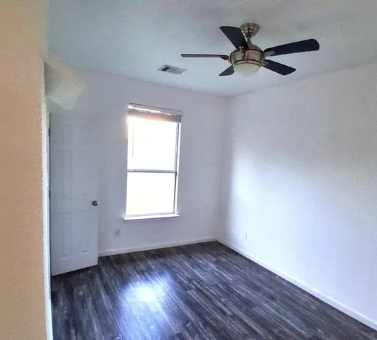 an empty room with wooden floor fan and windows