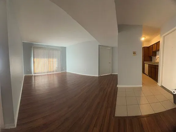 a view of empty room with wooden floor and kitchen