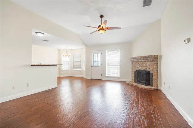 an empty room with wooden floor fireplace and windows