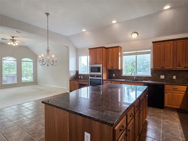 a kitchen with kitchen island granite countertop a stove a sink a counter space and living room view