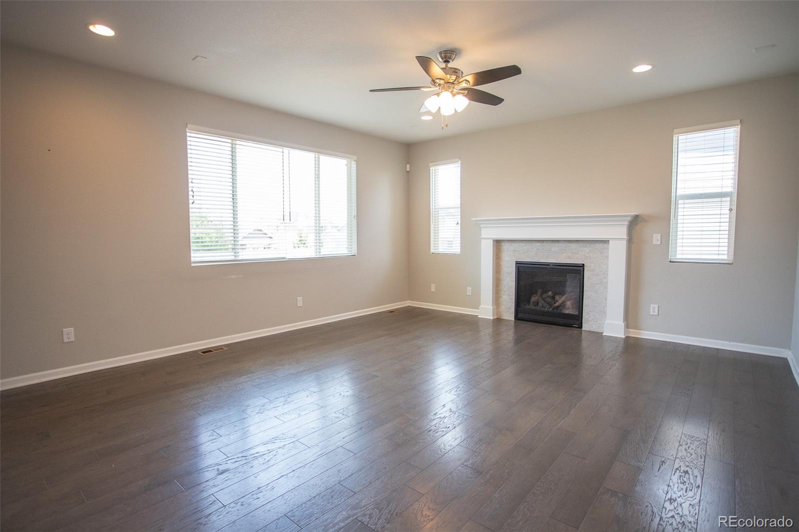 16343 East 100th Way Commerce City, CO 80022 - Photo 4 of 38 an empty room with wooden floor fireplace and windows