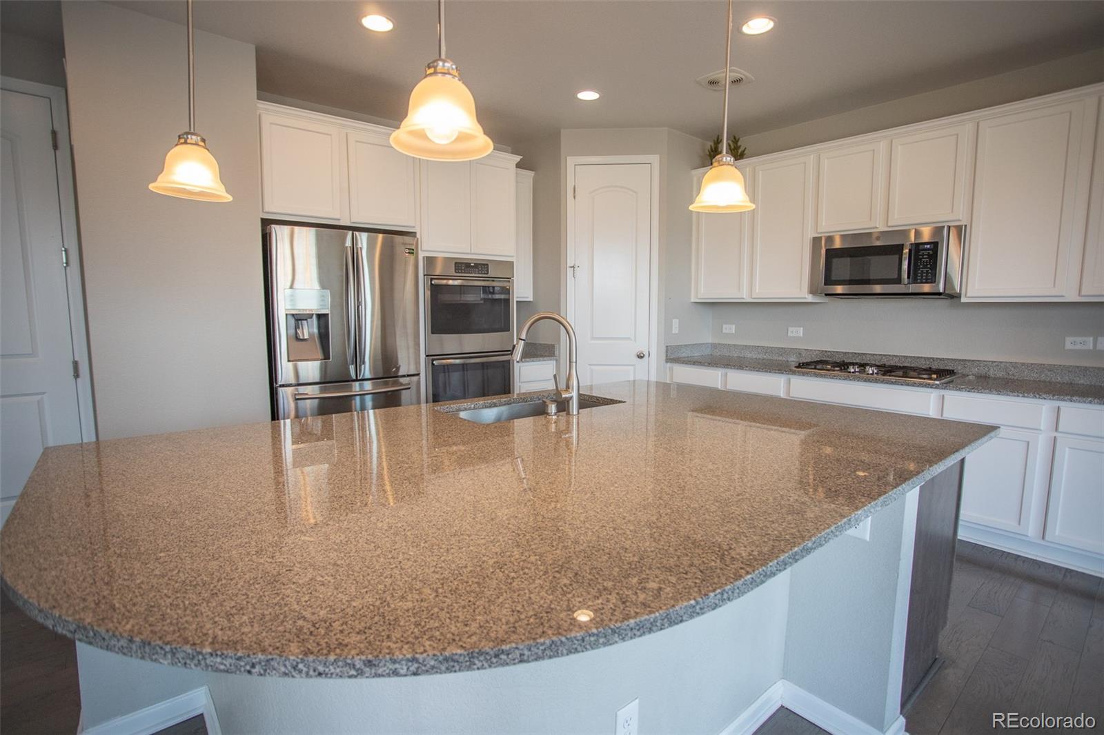 16343 East 100th Way Commerce City, CO 80022 - Photo 7 of 38 a large kitchen with kitchen island a large counter top stainless steel appliances and cabinets
