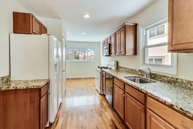 a kitchen with granite countertop a refrigerator a sink and wooden cabinets