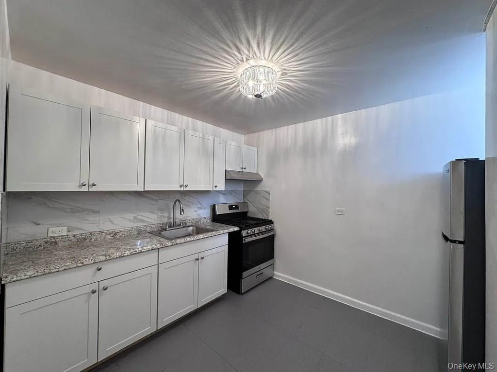 5639 Netherland Avenue, Unit 1B Bronx, NY 10471 - Photo 3 of 8 Kitchen featuring appliances with stainless steel finishes, light stone countertops, backsplash, white cabinetry, and a chandelier