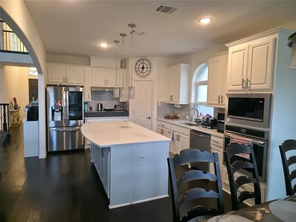 a kitchen with stainless steel appliances granite countertop a stove top oven a sink dishwasher and a refrigerator with wooden floor