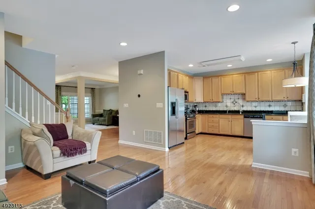 a living room with stainless steel appliances kitchen island granite countertop a refrigerator a stove a sink dishwasher and white cabinets with wooden floor