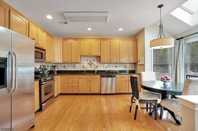 a kitchen with stainless steel appliances granite countertop a refrigerator a stove top oven a sink dishwasher a dining table and chairs with wooden floor