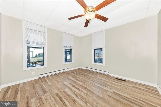 an empty room with wooden floor chandelier fan and windows
