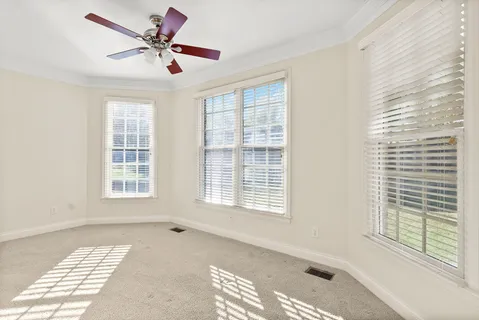 an empty room with chandelier fan and windows