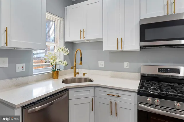a kitchen with stainless steel appliances a sink dishwasher stove and white cabinets with wooden floor