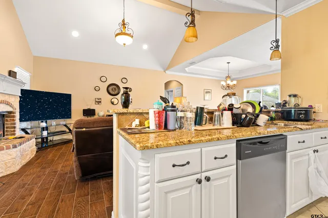 a kitchen with stainless steel appliances granite countertop a sink dishwasher and a flat tv screen with wooden floor