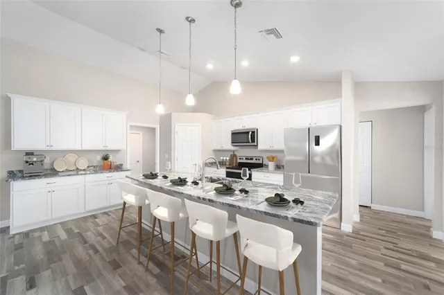 a kitchen with stainless steel appliances kitchen island granite countertop a sink a stove a refrigerator cabinets and chairs