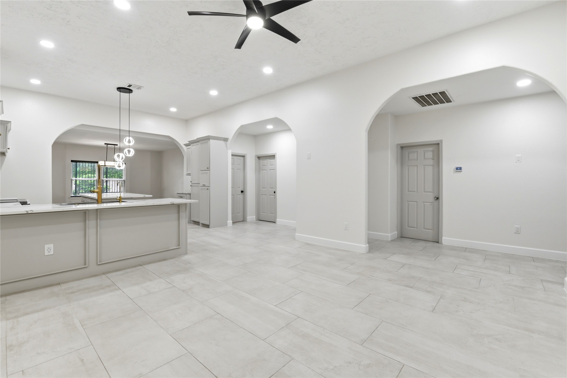 9403 Spaulding Street Houston, TX 77016 - Photo 9 of 50 This spacious, modern kitchen features sleek white cabinetry, a large island with a breakfast bar, and stylish pendant lighting. The open layout, with arched doorways and light-colored tile flooring, creates an inviting and airy atmosphere, perfect for entertaining.