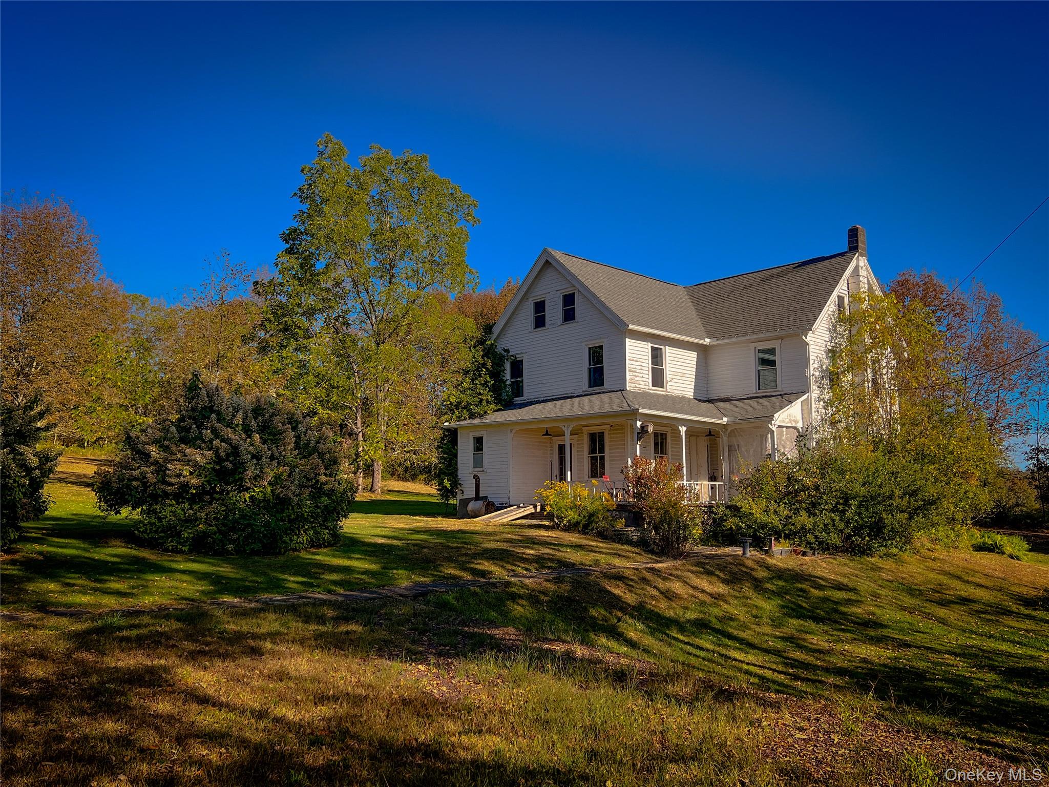 View of side of home with a porch, a yard, a chimney, and roof with shingles