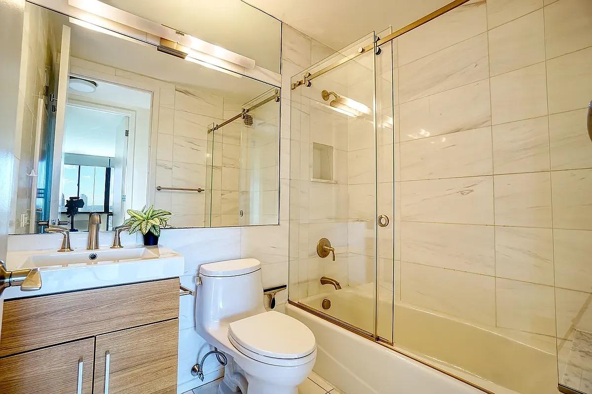 255 East 49th Street, Unit 31C Manhattan, NY 10017 - Photo 7 of 11 a bathroom with a shower a sink a toilet and a mirror