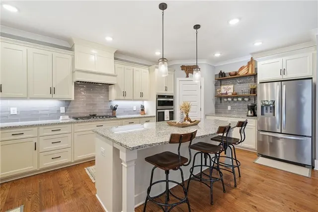 a kitchen with stainless steel appliances granite countertop a refrigerator a sink dishwasher a stove and white cabinets with wooden floor