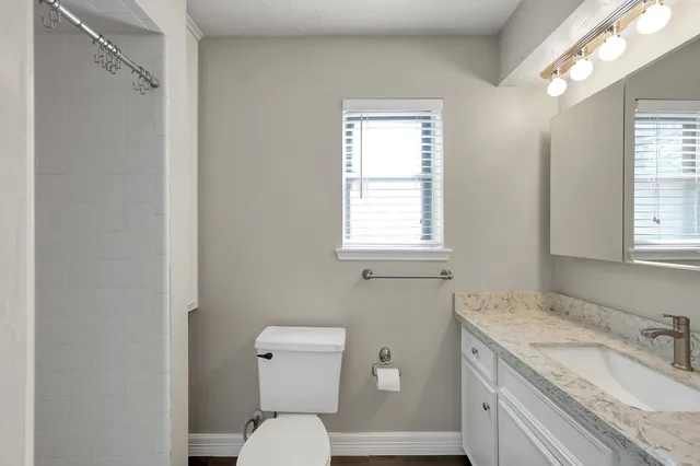 a bathroom with a granite countertop toilet a sink and a window
