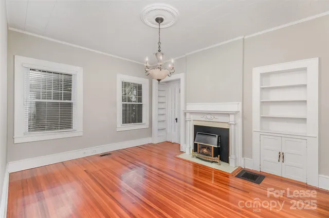 a view of an empty room with wooden floor fireplace and a window