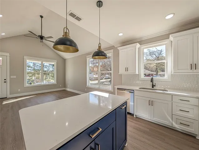 a kitchen with stainless steel appliances kitchen island a white stove a sink a refrigerator and white cabinets with wooden floor