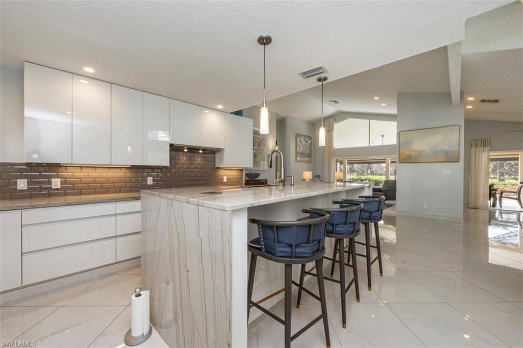 550 Cormorant Cove Naples, FL 34113 - Photo 6 of 39 a kitchen with kitchen island a dining table chairs and white cabinets