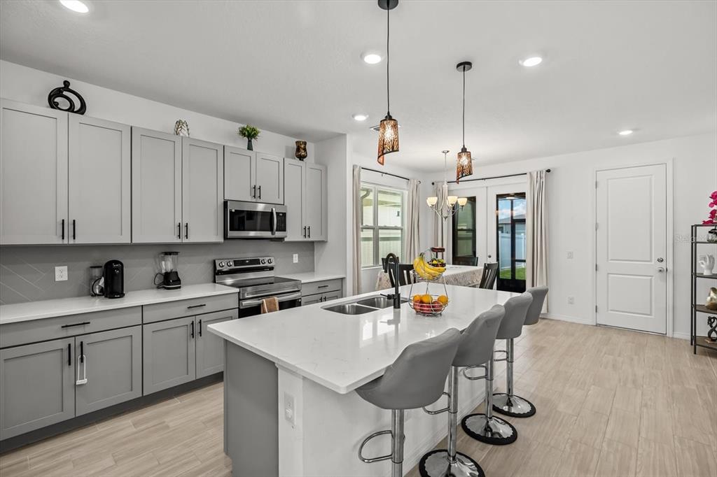17061 Seville Orange Road Winter Garden, FL 34787 - Photo 5 of 42 a open kitchen with stainless steel appliances granite countertop a stove a sink a kitchen island a dining table and chairs with wooden floor