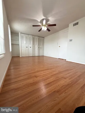an empty room with wooden floor ceiling fan and windows