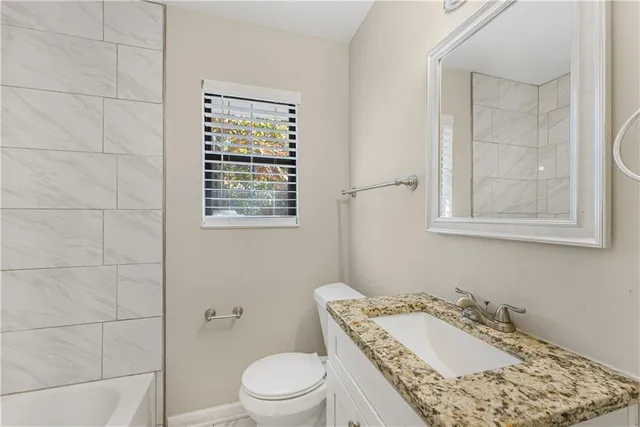 a bathroom with a granite countertop bathtub sink vanity mirror and toilet