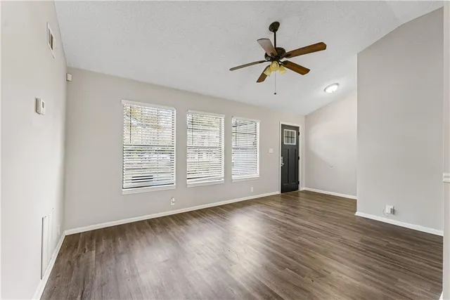 an empty room with wooden floor fan and windows