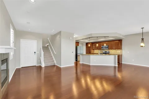 a view of an empty room with wooden floor and a kitchen