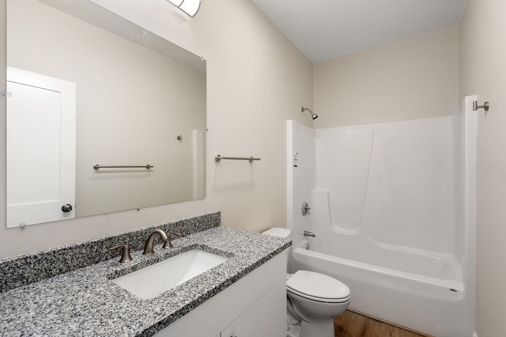 242 Main Street, Unit 203 Millis, MA 02054 - Photo 10 of 18 a bathroom with a granite countertop toilet a sink and a mirror
