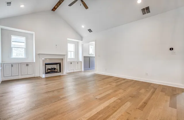 an empty room with wooden floor fireplace and windows