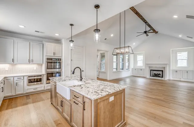 a large kitchen with kitchen island a stove a sink a refrigerator and white cabinets with wooden floor