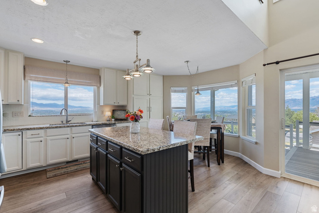 14883 Tooele Lane Draper, UT 84020 - Photo 17 of 49 Open-concept kitchen featuring an eat-at island with granite countertop, wood-finish flooring, white cabinetry, and a full suite of windows providing abundant natural light