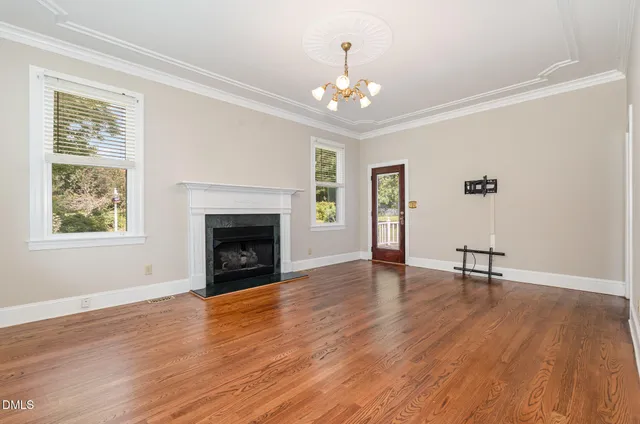 a view of an empty room with wooden floor fireplace and a window
