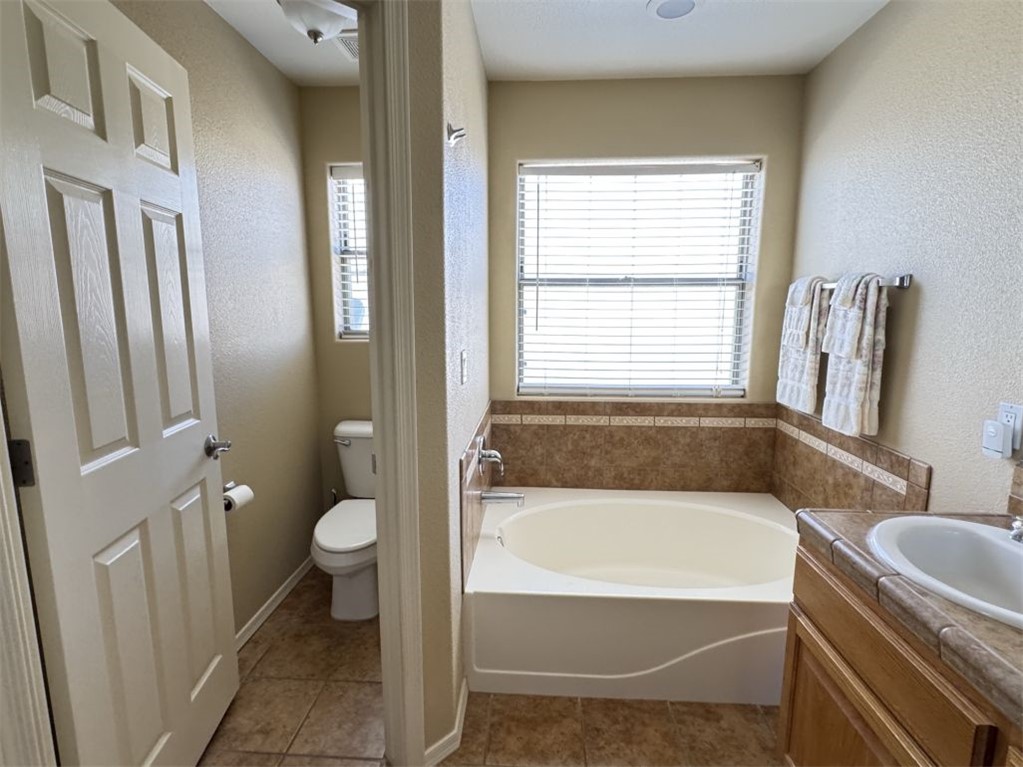 3316 Producers Mine Road Kingman, AZ 86401 - Photo 26 of 35 Bathroom featuring a built-in soaking tub with tile surround, a single vanity with a tile countertop, a separate water closet, and tile flooring