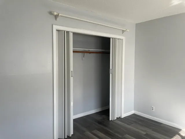 a view of an empty room with wooden floor and closet