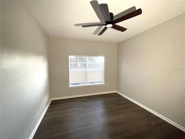 an empty room with wooden floor ceiling fan and windows