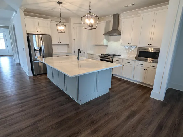 a kitchen with stainless steel appliances granite countertop a sink a stove a refrigerator and island with wooden floor