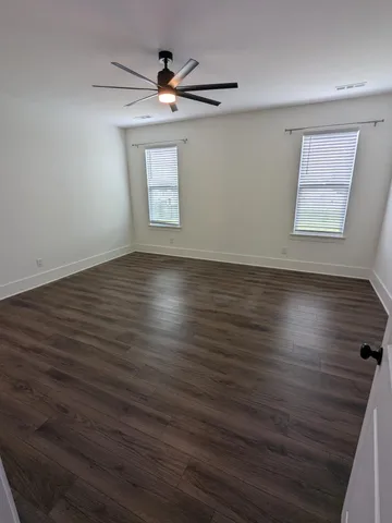 an empty room with wooden floor fan and windows
