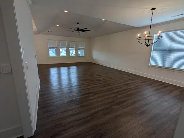 an empty room with wooden floor staircase and windows
