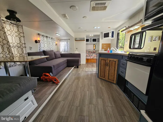 a living room with stainless steel appliances kitchen island granite countertop a refrigerator a stove a microwave oven with white cabinets and wooden floor