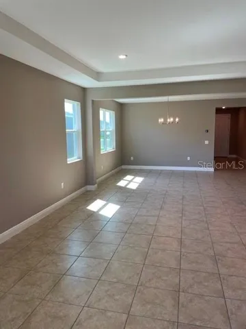 a view of an empty room with window and chandelier fan