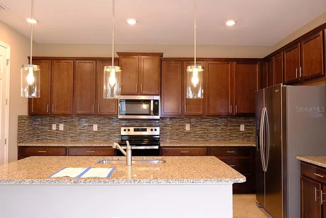 a kitchen with kitchen island granite countertop a refrigerator a stove a sink a washer dryer and white cabinets