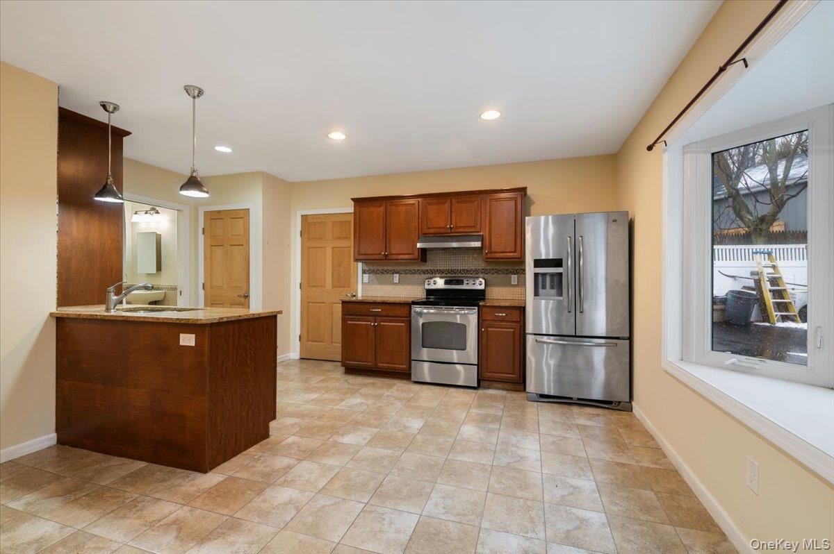 33 Fleets Cove Road Huntington, NY 11743 - Photo 4 of 42 Apartment Kitchen featuring stainless steel appliances, decorative backsplash, hanging light fixtures, brown cabinets, and light stone countertops