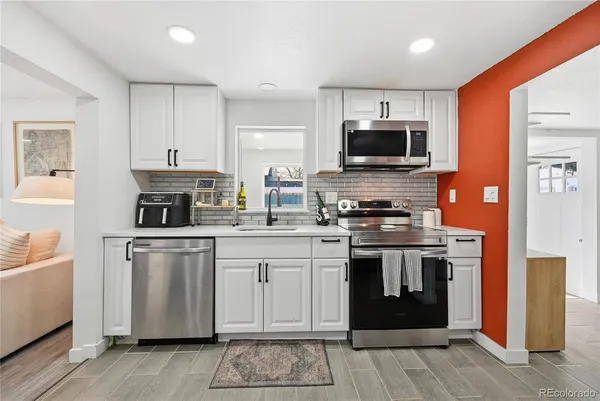 a kitchen with stainless steel appliances granite countertop a stove top oven a sink dishwasher and a refrigerator with wooden floor